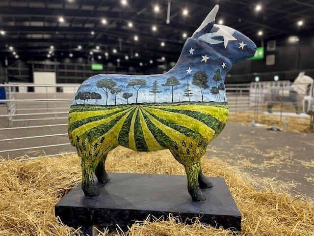 Sheep statue painted to depict a field with trees and a blue sky