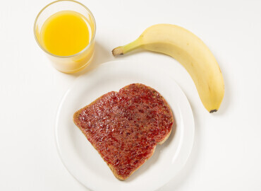 Glass of fresh orange juice, a slice of toast with jam, banana