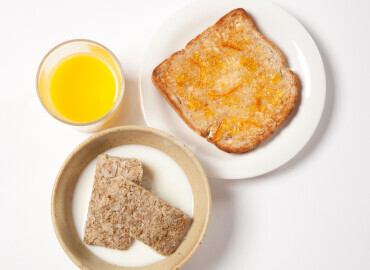 Bowl of wheat bisks, slice of wholemeal toast and marmalade, and a glass of fresh orange juice