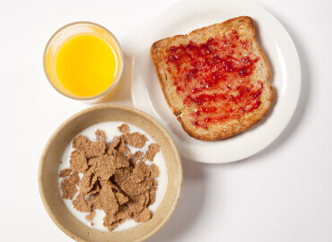 Bowl of wholegrain breakfast flakes, slice of wholemeal toast and jam, and glass of fresh orange juice