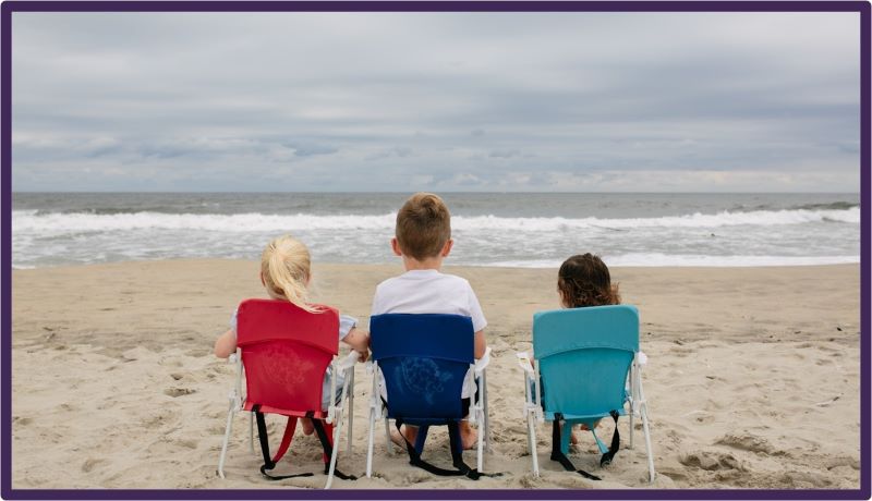 Three children sitting on chairs at the beach looking out to the sea