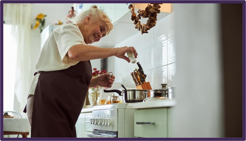 Older lady with white hair smiling as she's cooking