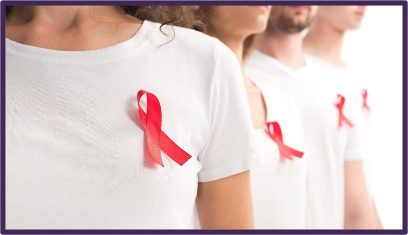 Three people standing wearing white t-shirts and a red ribbon for HIV awareness.