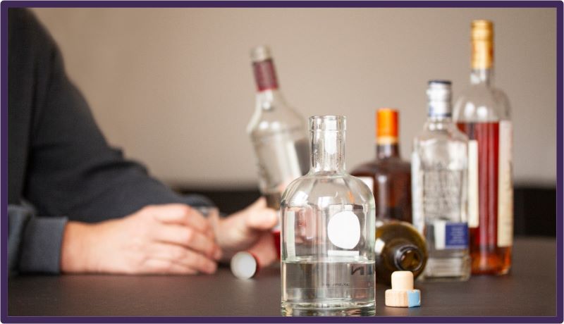 A person sitting at a table with multiple bottles of alcohol.
