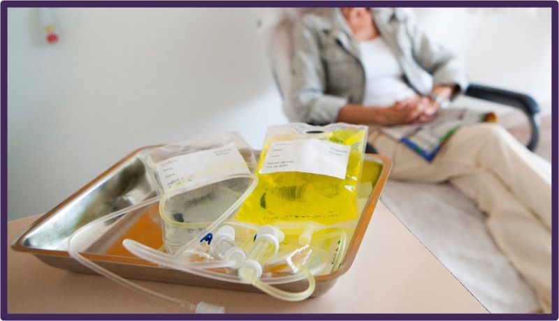 Person lying on a bed with two bags of chemotherapy medicine beside them.