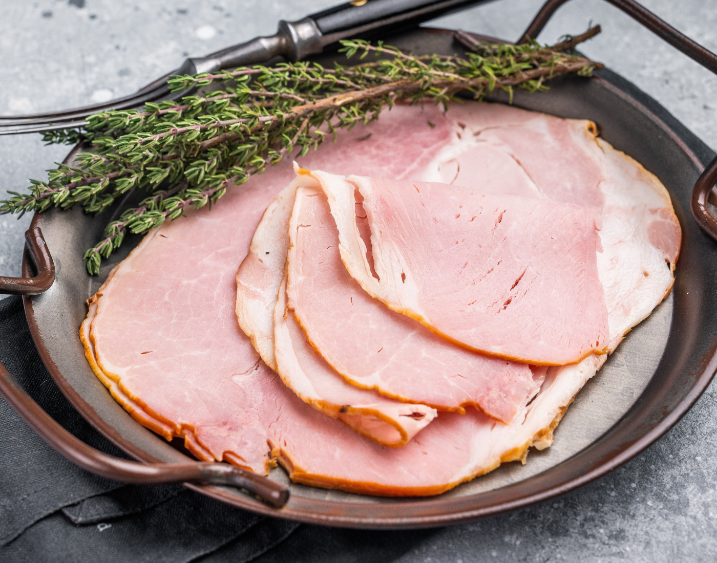 slices of ham on a steel dish with sprigs of thyme off to the side. 