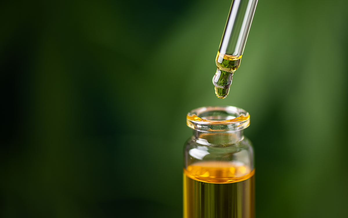 Oil in glass vial with eye dropper with a green background.