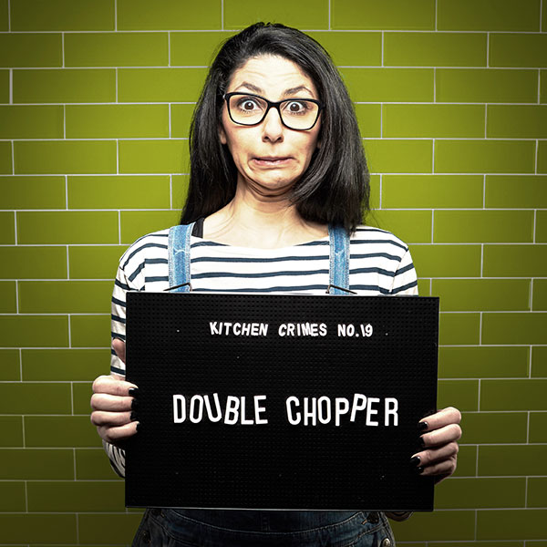 Mock mug shot photograph of a woman holding a sign saying kitchen crimes number 19: double chopper