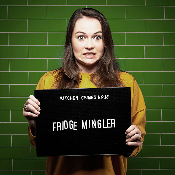 Mock mug shot photograph of a woman holding a sign saying kitchen crimes number 13: fridge mingler 