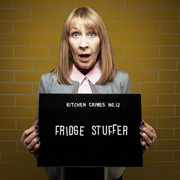 Mock mug shot photograph of a woman holding a sign saying 'kitchen crimes number 12: fridge stuffer' 