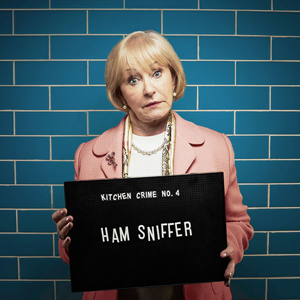 Mock mug shot photograph of a woman holding a sign saying 'kitchen crimes number four: 'ham sniffer' 