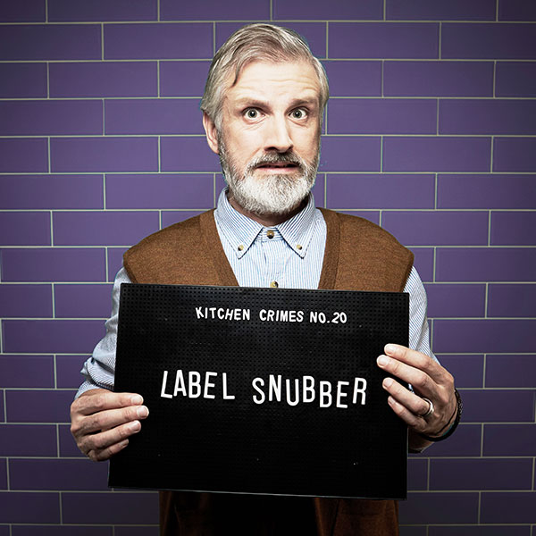 Mock mug shot photograph of a man holding a sign saying kitchen crimes number 20: label snubber