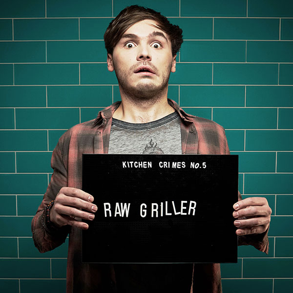 Mock mug shot photograph of a man holding a sign saying 'kitchen crimes number five: raw griller' 
